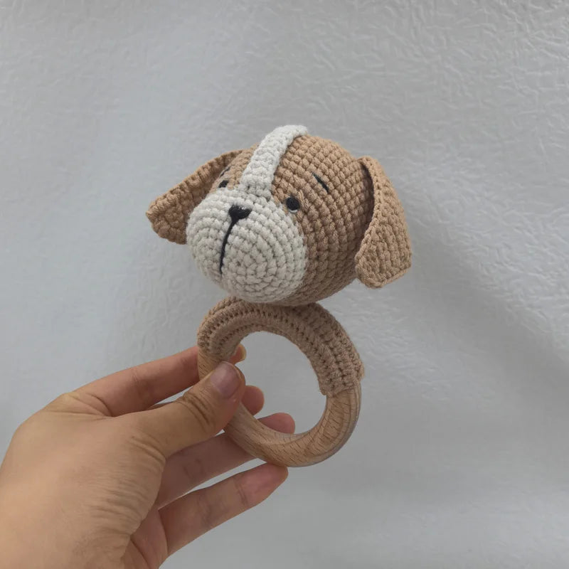 A handcrafted wooden baby rattle and teether ring shaped like a dog, made of light brown and white yarn.