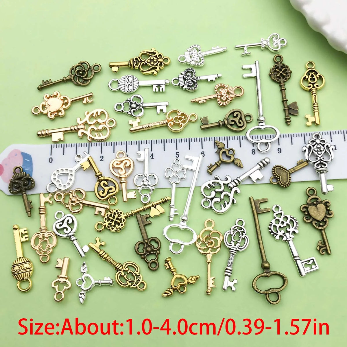 A collection of vintage brass and silver key charms for jewelry making displayed on a ruler.