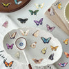 A collection of colorful butterfly stickers arranged on a white plate and wooden surface.