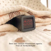 A black digital thermometer is held in a hand resting on a soft, light-colored fabric.