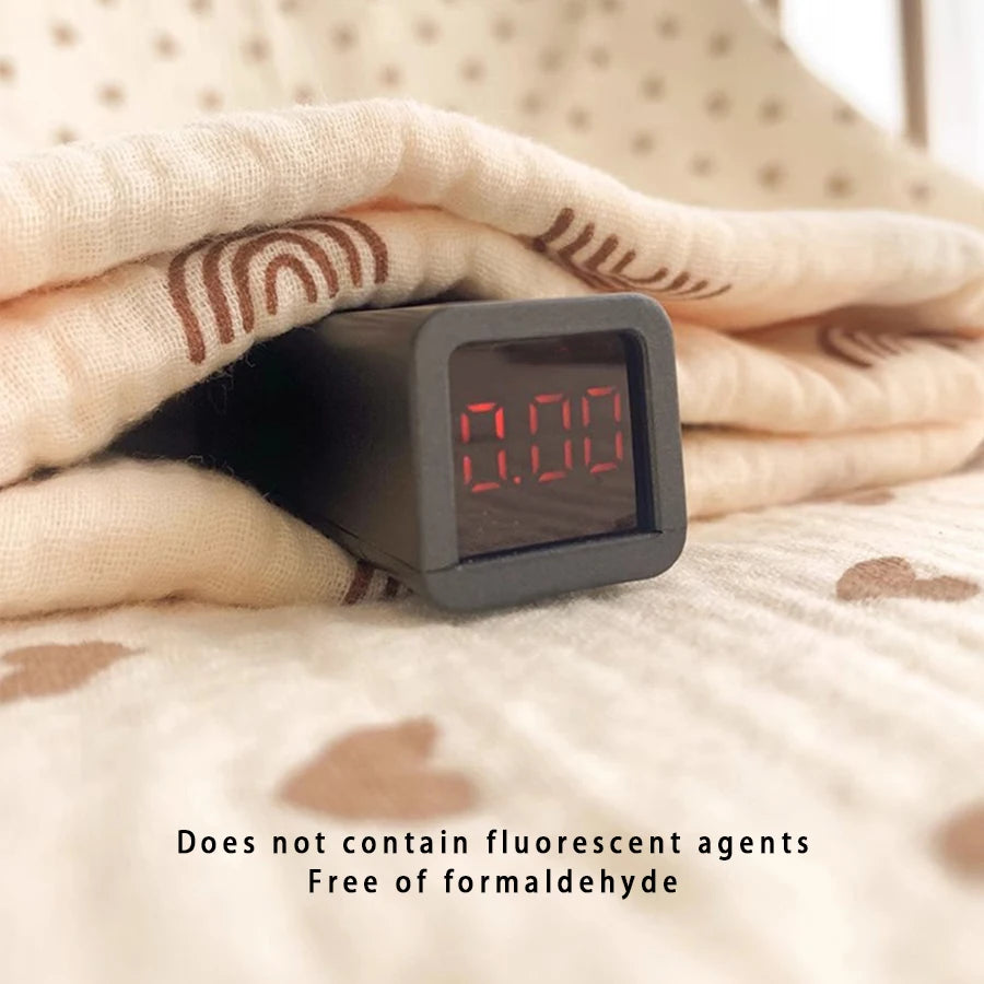 A black digital thermometer is held in a hand resting on a soft, light-colored fabric.
