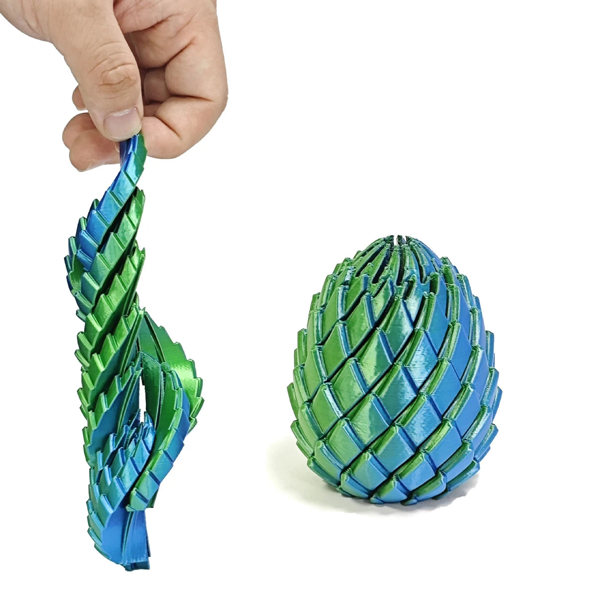 A hand holds a green and blue expandable dragon egg fidget toy with textured scales.