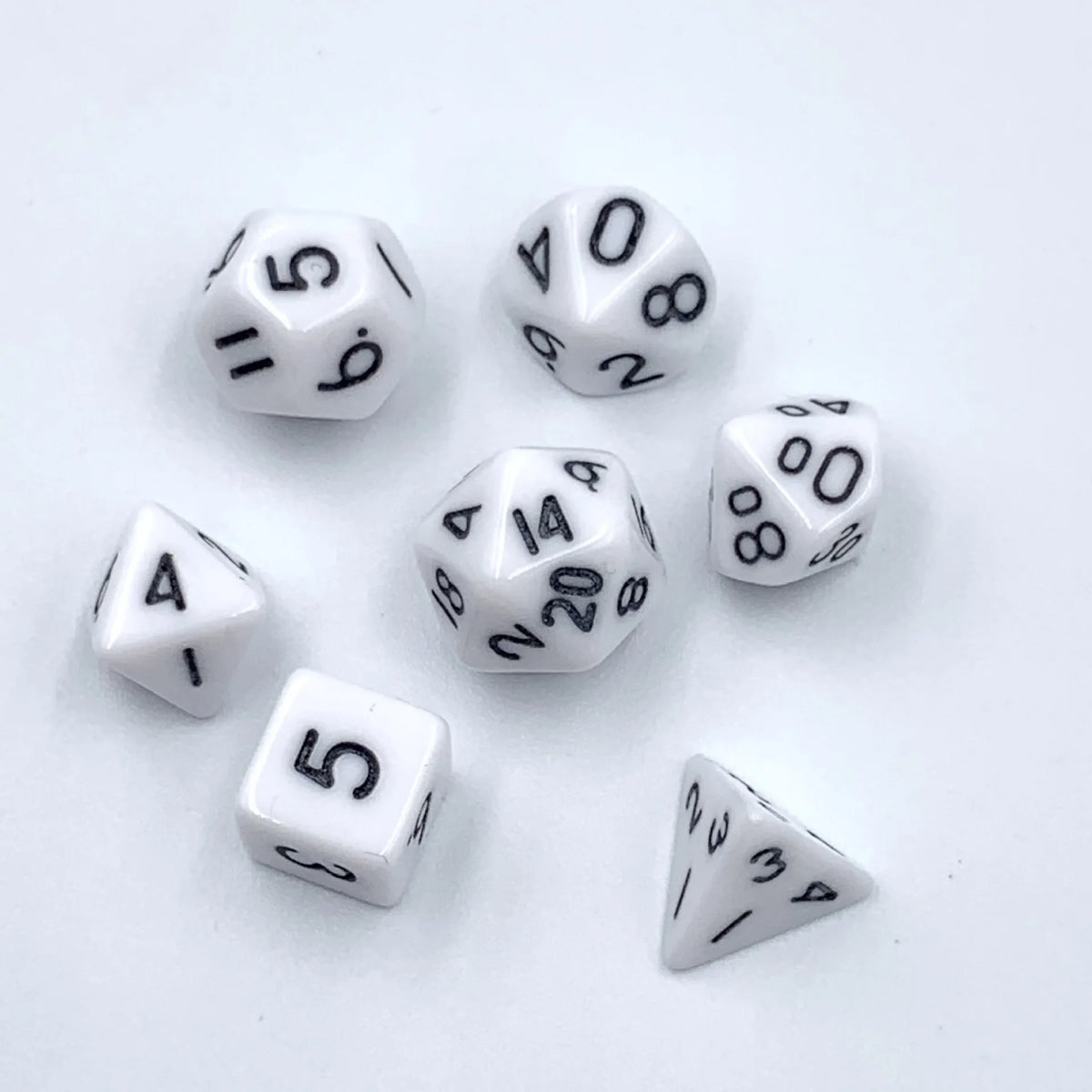 A collection of seven white acrylic dice, including d6 and d8 shapes, scattered on a white surface.