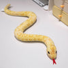 A yellow lifelike simulation snake plush toy is coiled on a white surface.