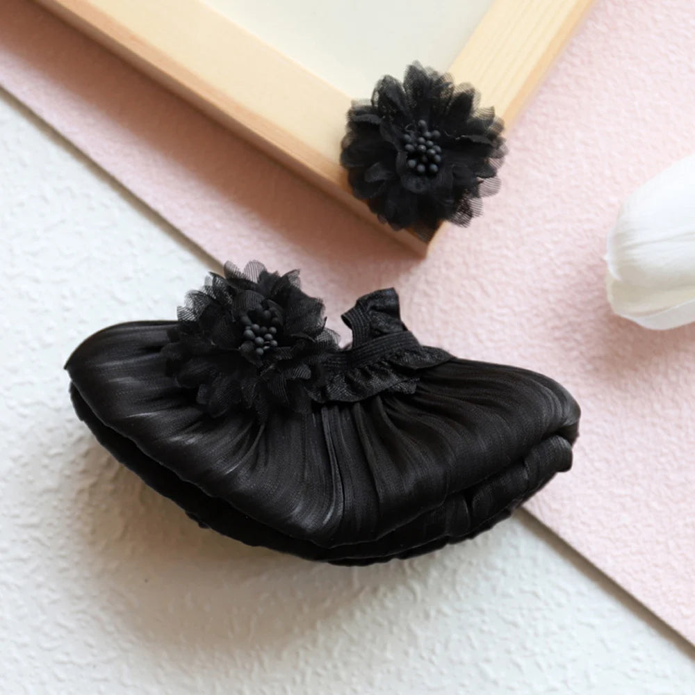 A black ruffled mini doll wedding dress outfit set with black floral embellishments displayed on a light pink surface.