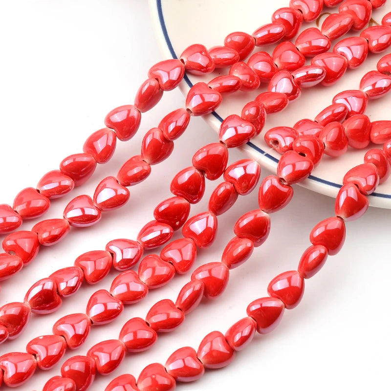 A string of bright red heart-shaped acrylic beads for jewelry making laid out on a white surface.