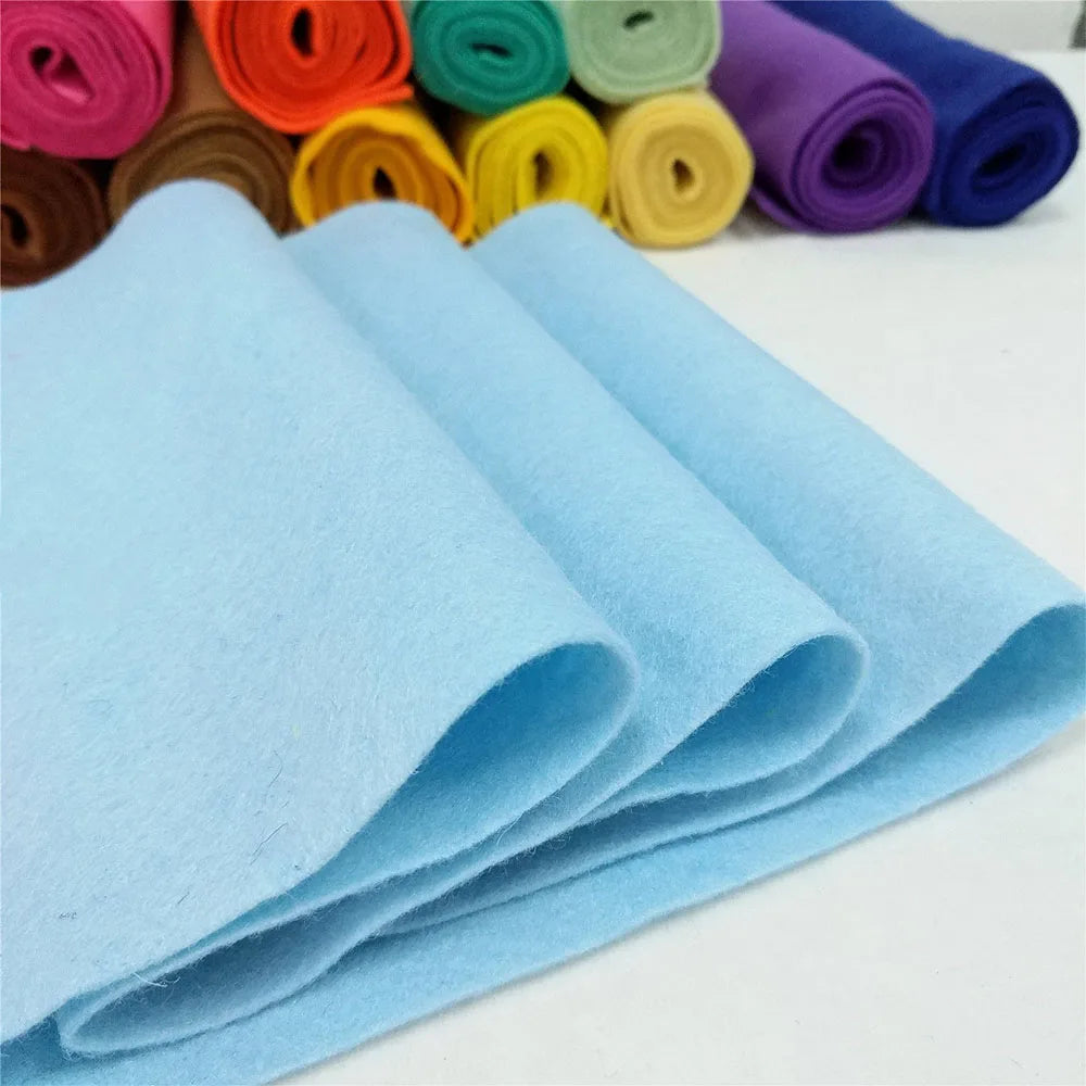 A stack of light blue felt fabric sheets rolled and laid out next to various colored felt rolls.