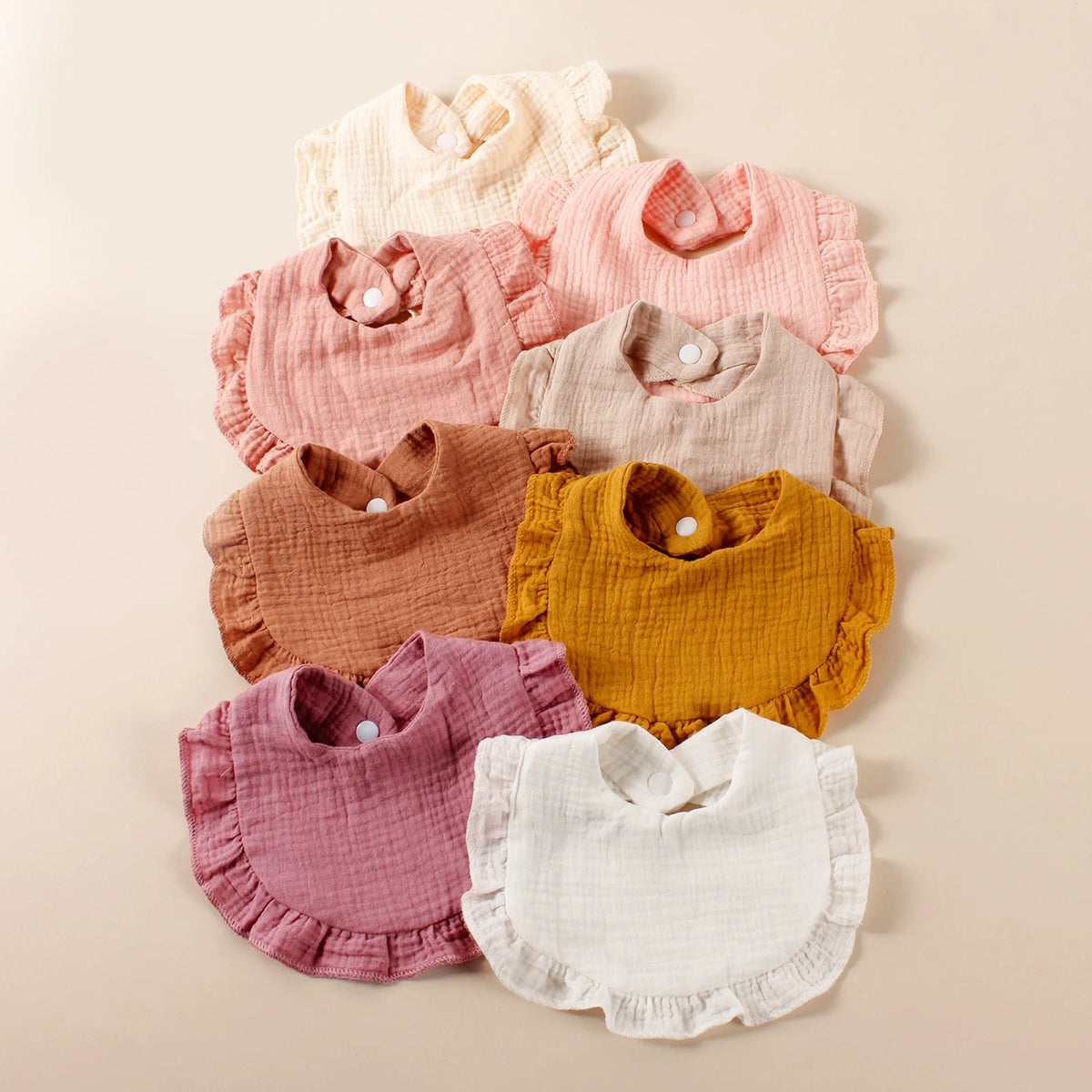 A stack of eight pink and peach cotton ruffle baby bibs in various shades of pink, peach, and yellow.