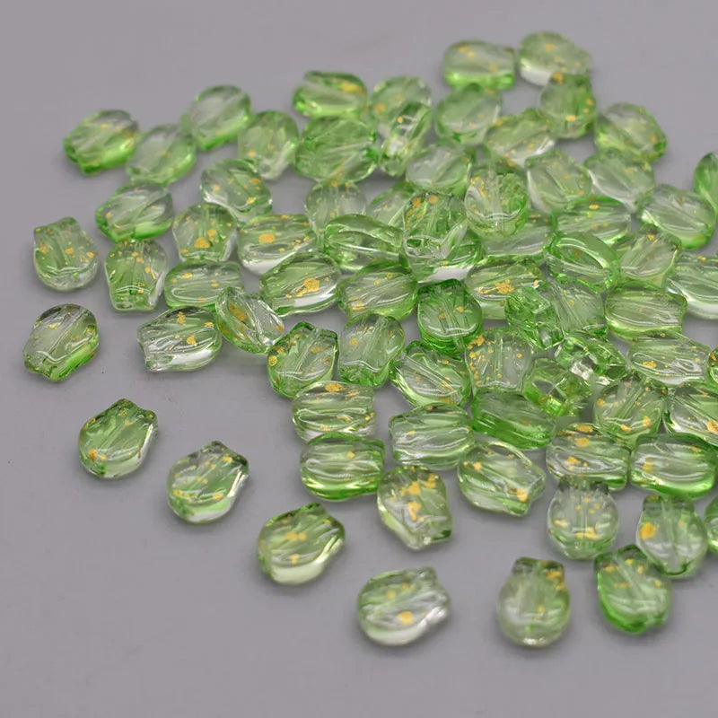 A pile of translucent green tulip flower glass beads scattered on a gray surface.