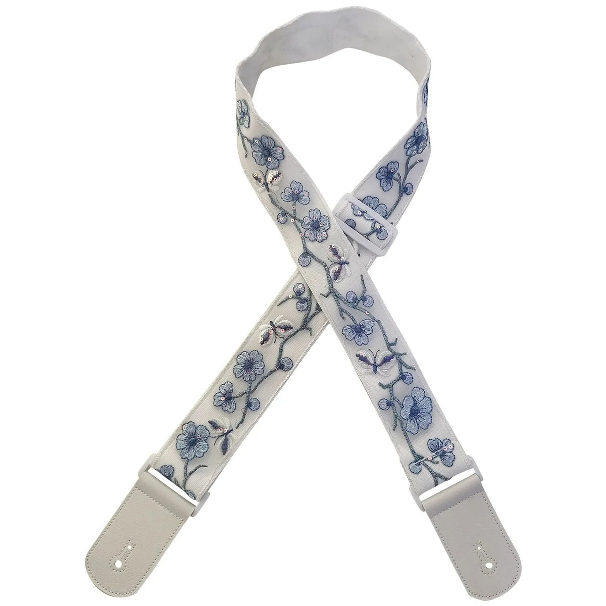 A beige woven guitar strap with blue floral embroidery and leather accents, shown in an X-shape.