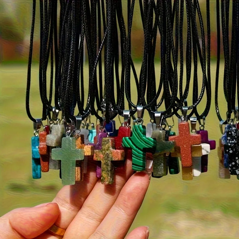 A hand holds a collection of natural stone cross pendants with various colors and textures.