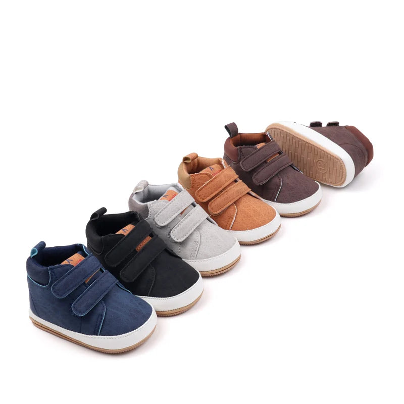 A row of brown, gray, and navy soft PU leather baby first walker shoes with anti-slip TPR soles.
