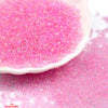 A close-up of pink glossy glass seed beads scattered on a white surface.