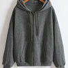 A gray oversized zip-up hoodie hanging on a wooden hanger against a white wall.