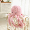 A pink and cream plush octopus toy with hanging loops displayed on a gold wire stand.
