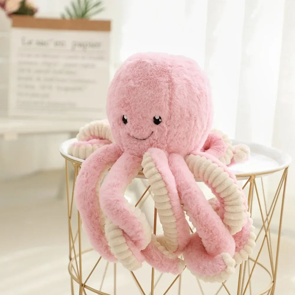 A pink and cream plush octopus toy with hanging loops displayed on a gold wire stand.