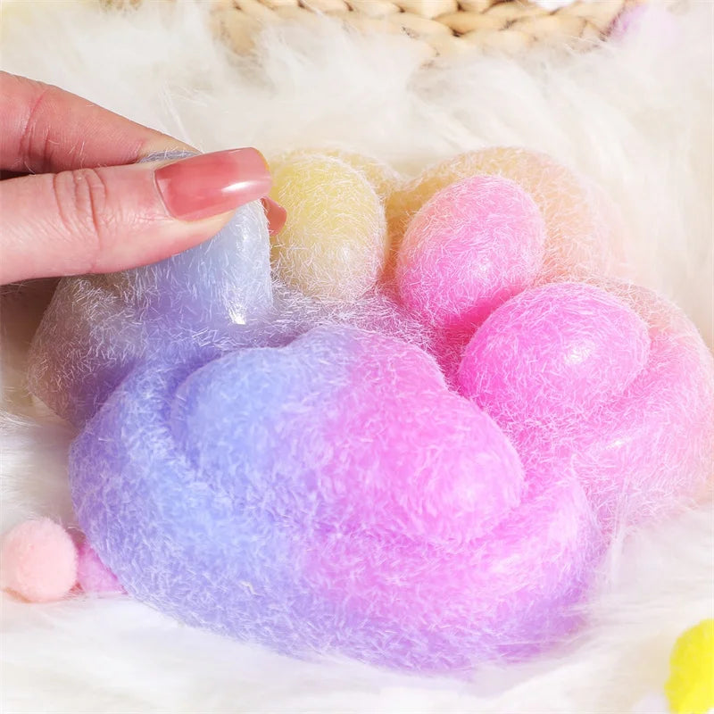 A hand holds a collection of colorful squishy toys shaped like cat paws, featuring pink, yellow, and purple hues.