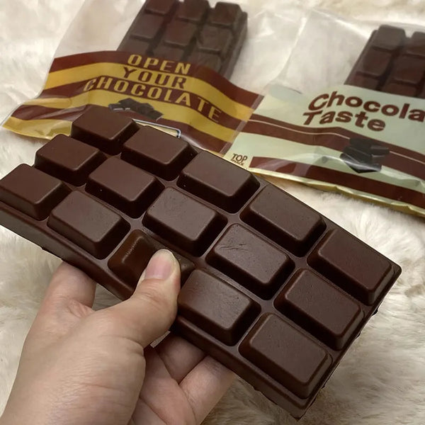 A hand holds a brown chocolate bar fidget toy with a grid pattern against a white fluffy background.