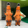 An adult inflatable T-Rex costume in orange and gray standing upright against a green wall.