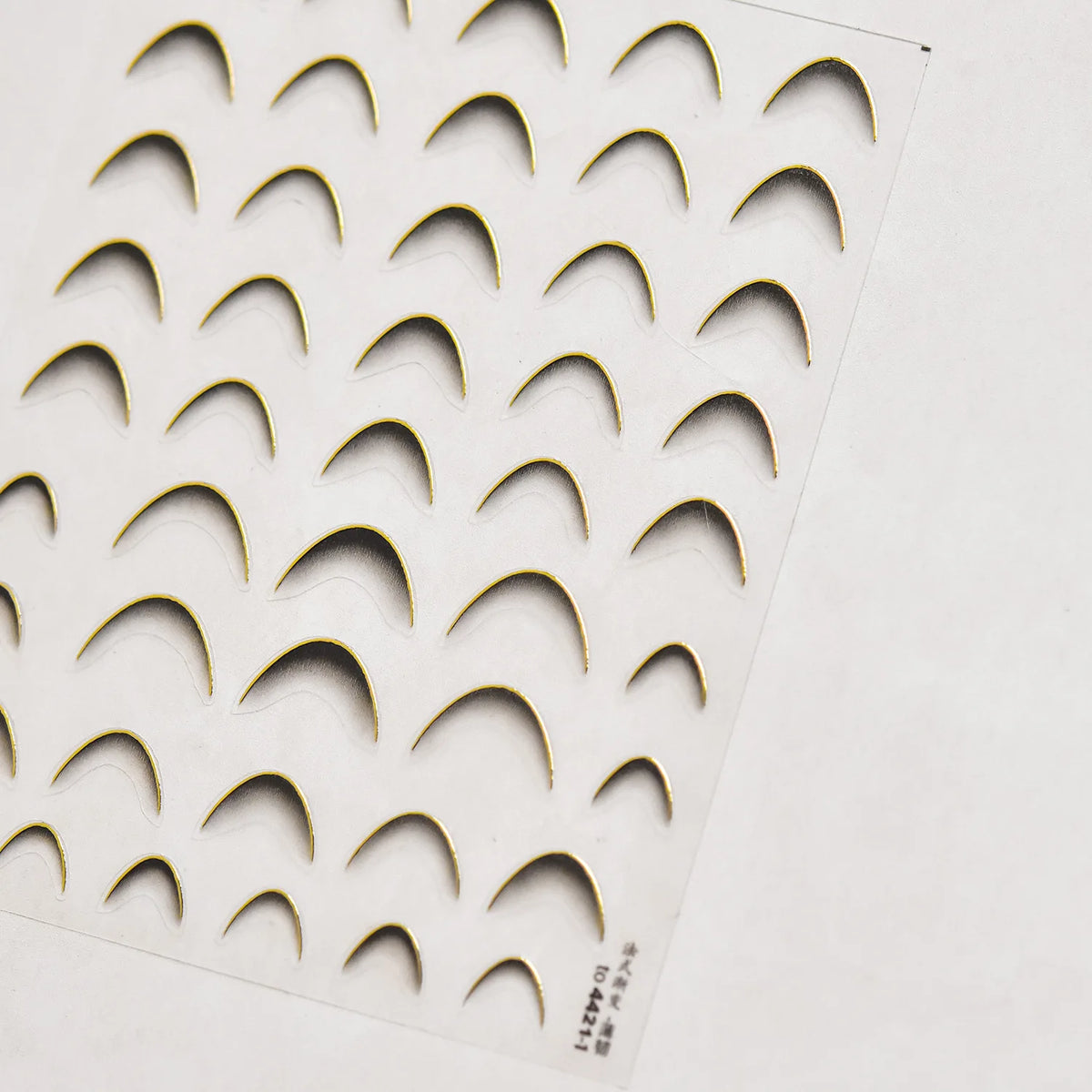 A sheet of gold-colored nail art stickers featuring a pattern of arched shapes.