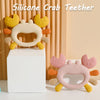 A silicone crab teether with yellow and orange claws and a pink body is displayed on a white block.
