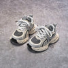 A pair of gray and white breathable mesh kids running sneakers with cushioned soles resting on a gray concrete surface.