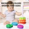 A baby is interacting with a colorful rainbow spinning stacking tower and various colored plastic rings.