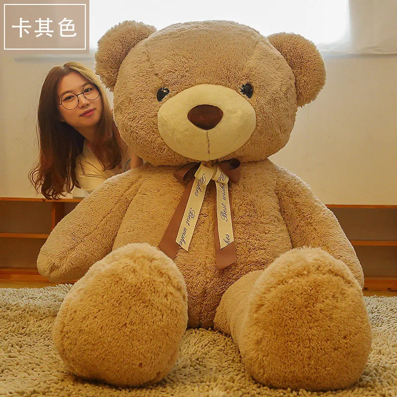 A large, light brown teddy bear plush toy sitting on a beige carpet next to a young woman.