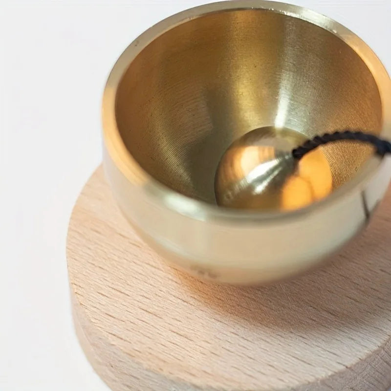A small brass singing bowl resting on a light wooden surface.