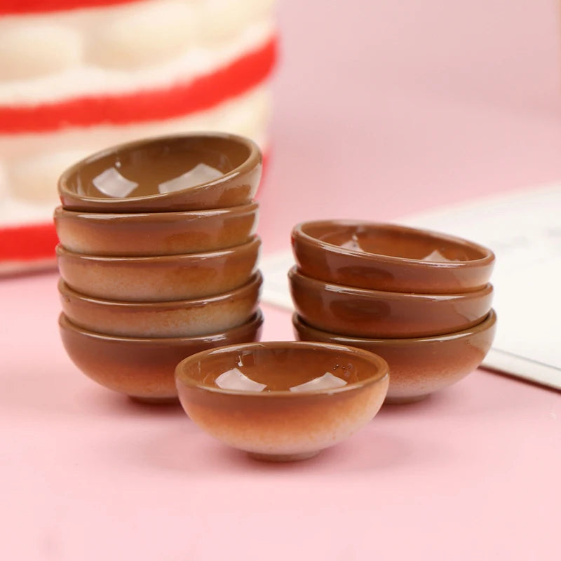 A set of ten miniature brown rice bowls arranged in a stack on a pink surface.