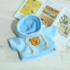 Light blue fleece hoodie with a tan bear patch and drawstring on a white wooden surface.