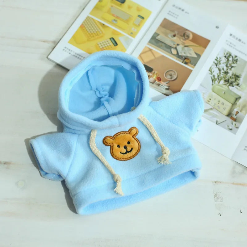 Light blue fleece hoodie with a tan bear patch and drawstring on a white wooden surface.