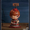 A collectible figurine of a character with reddish-brown hair and a red hat, standing on a brown surface.