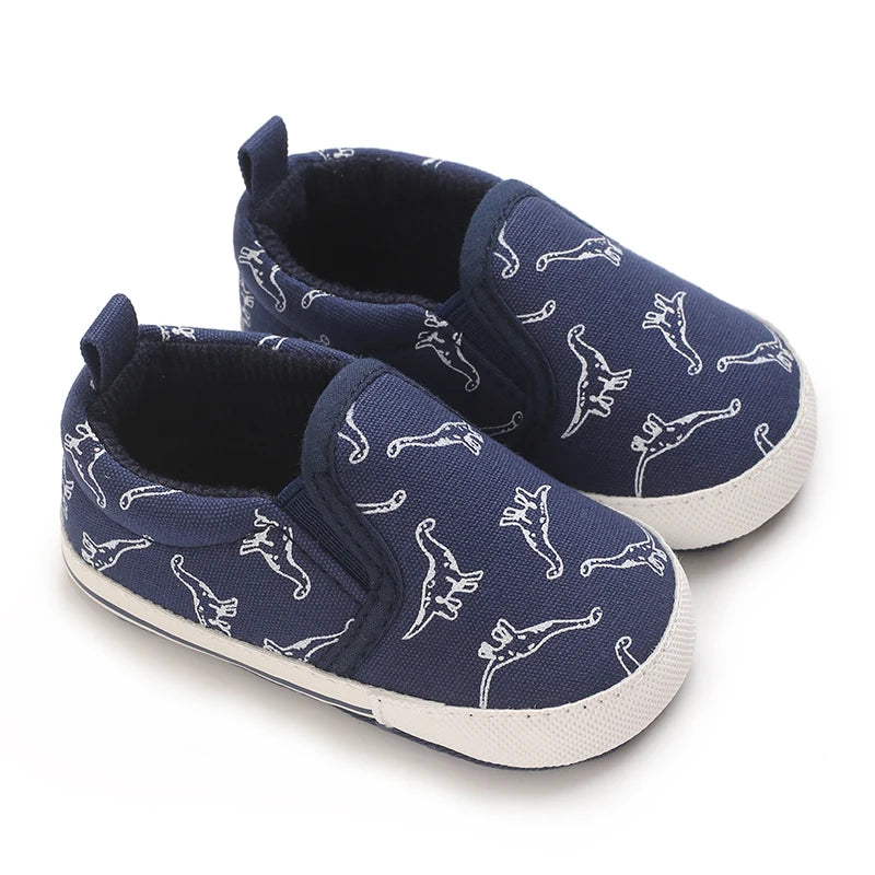 A pair of navy blue baby first walker sneakers featuring a white dinosaur print.