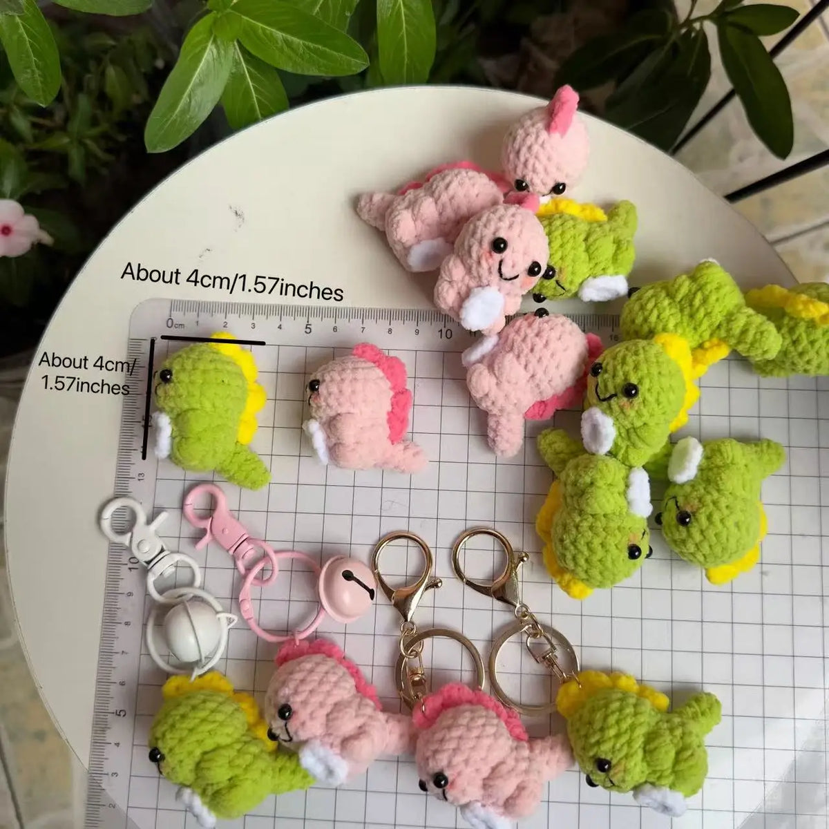 A collection of handmade crochet dinosaur keychains in various shades of pink, green, and yellow.
