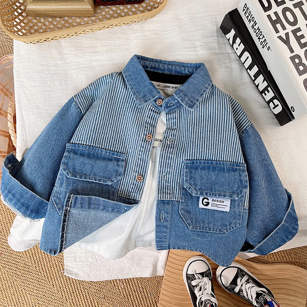 A blue and white striped denim jacket laid flat on a white cloth next to a stack of books.