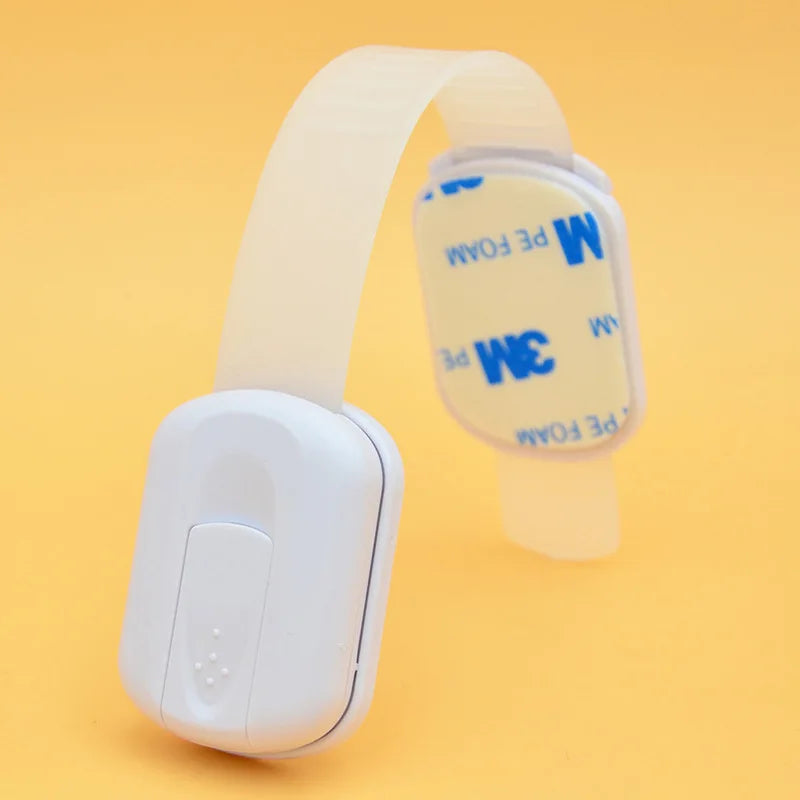 A white adhesive baby safety lock featuring a clear strap and blue lettering on the plastic component.
