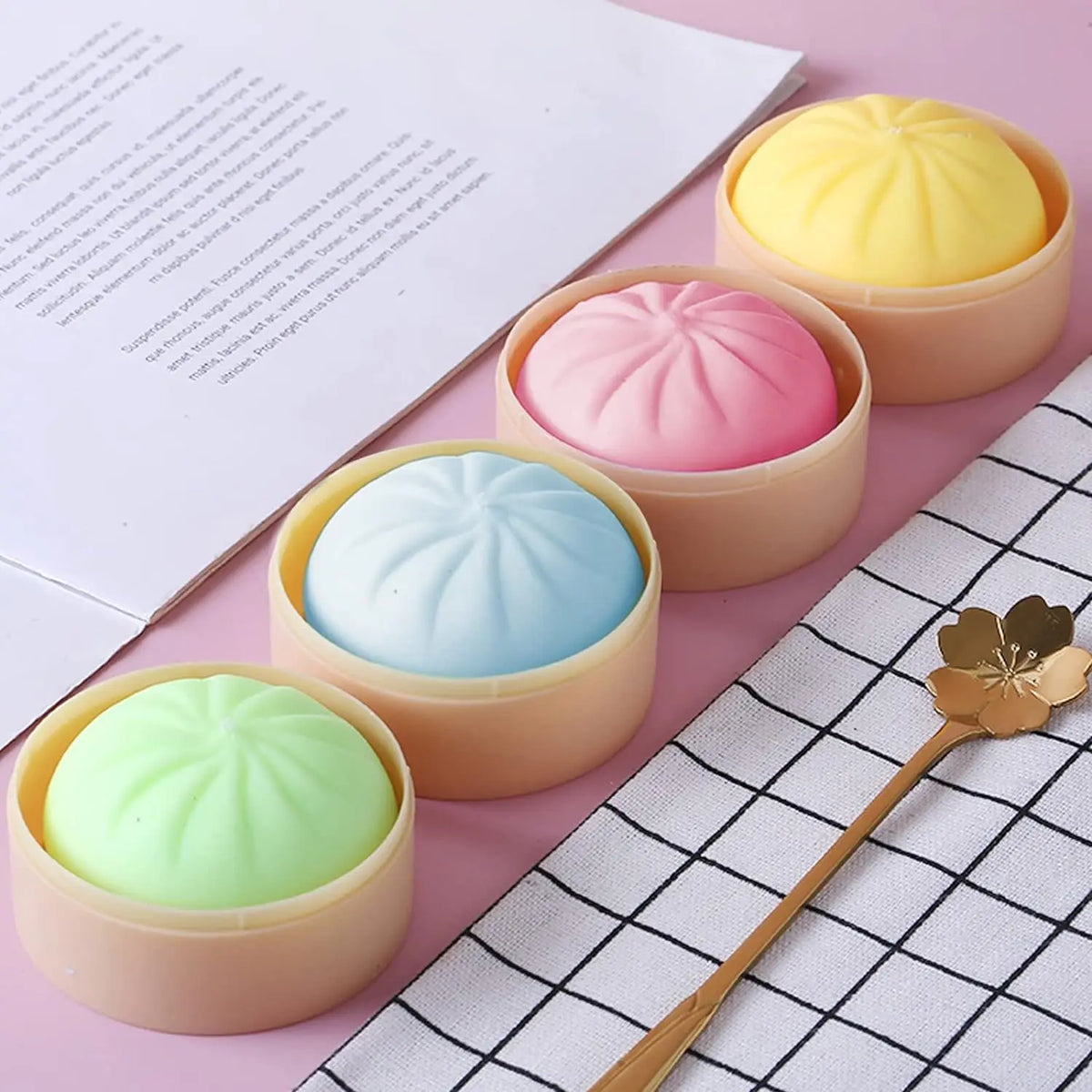A set of five pastel-colored dumpling squishy stress balls in various shades of pink, yellow, and blue resting on a checkered