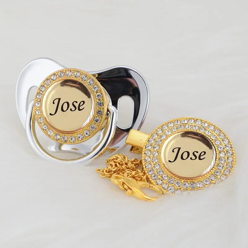 A gold and silver crystal pacifier and clip set featuring the name Jose