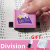 A pink math roller stamp with a purple design is being held over a grid of division problems.