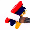A paintbrush with thick strokes of red, blue, and yellow acrylic paint on a white background.