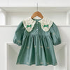 A teal cotton party dress for girls featuring lace collar details and embroidered motifs, displayed on a wooden hanger.