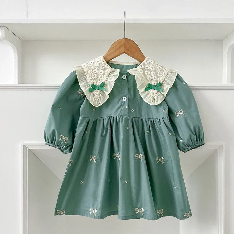 A teal cotton party dress for girls featuring lace collar details and embroidered motifs, displayed on a wooden hanger.