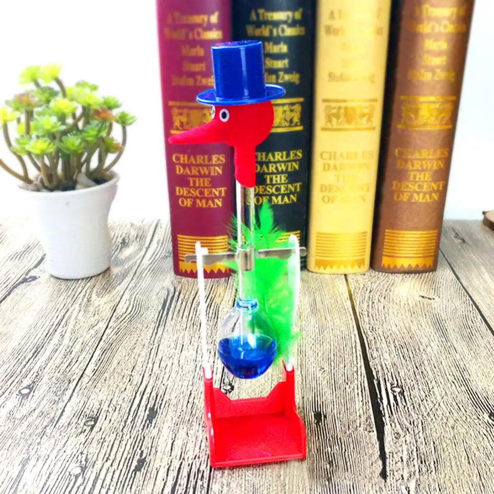A red bird toy with a glass bulb and green accents sits in front of several books.