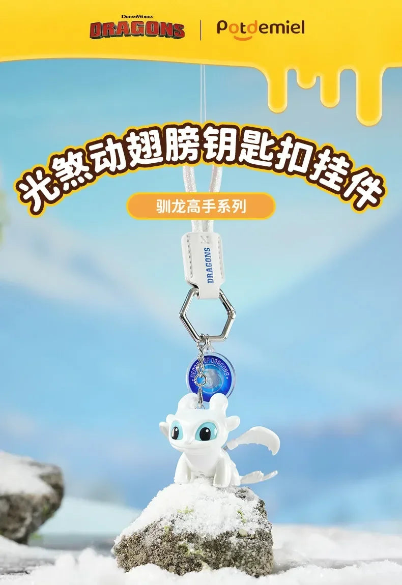 A white Toothless Dragon keychain with movable wings and glowing eyes is displayed on a snowy rock.