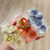 Three glass bottles filled with colored liquid and fruit pieces are held by a hand.