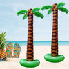 Two oversized inflatable palm trees with green fronds and brown trunks on a sandy beach.