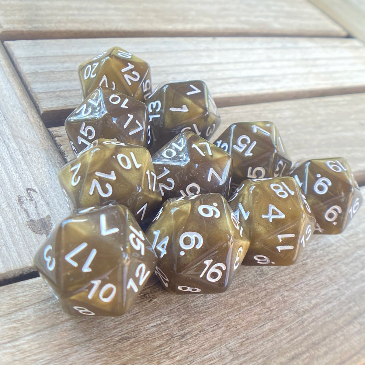 A collection of ten translucent amber pearl acrylic D20 dice scattered on a light wooden surface.