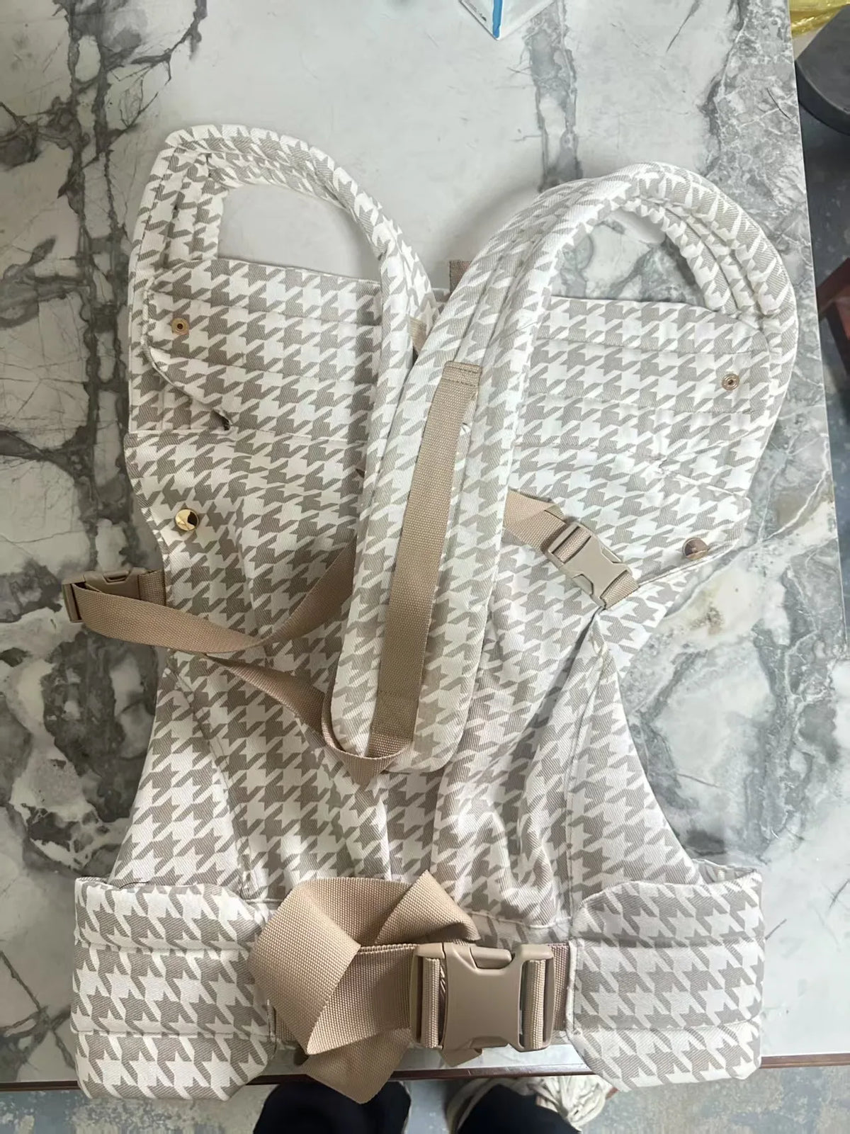 A beige and white patterned adjustable cotton baby carrier wrap laid out on a marble surface.