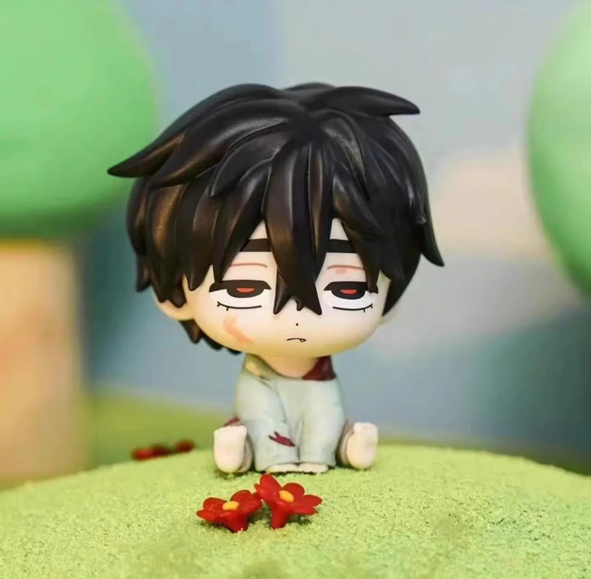 A black-haired mini figure collectible with red eyes and a white outfit sits on green textured surface.